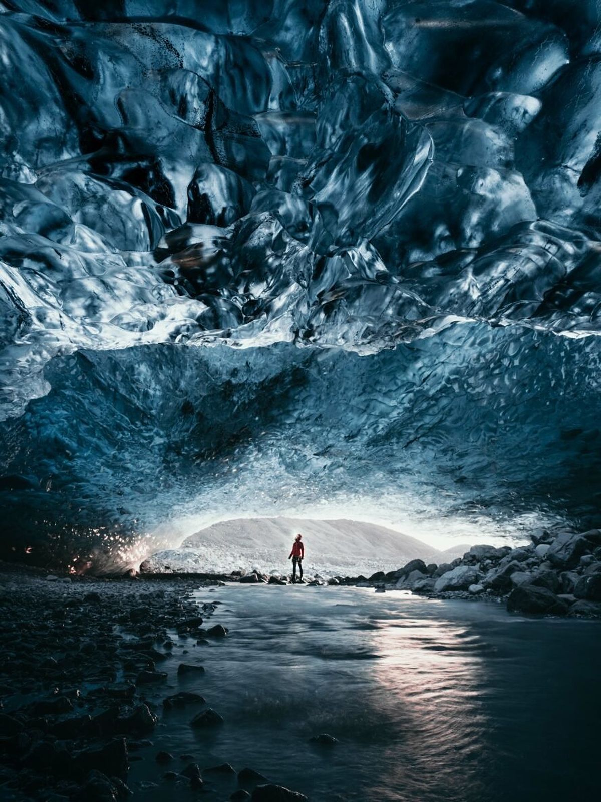 Hiker standing inside a glimmering blue ice cave in Iceland